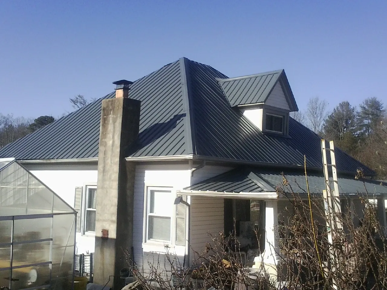 Dark blue standing seam metal roof on a white farmhouse with dormer — Slate & Tile Roof Repair by Roofing Brothers in Bethpage