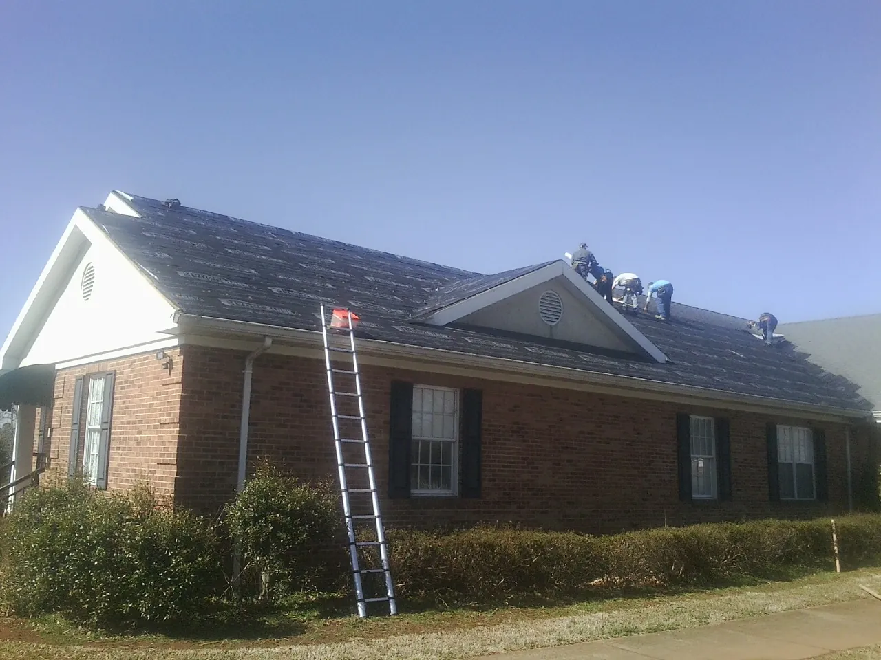 Crew tearing shingles off a brick ranch roof with a ladder set — Metal Roof Repair work by our crew in Bethpage