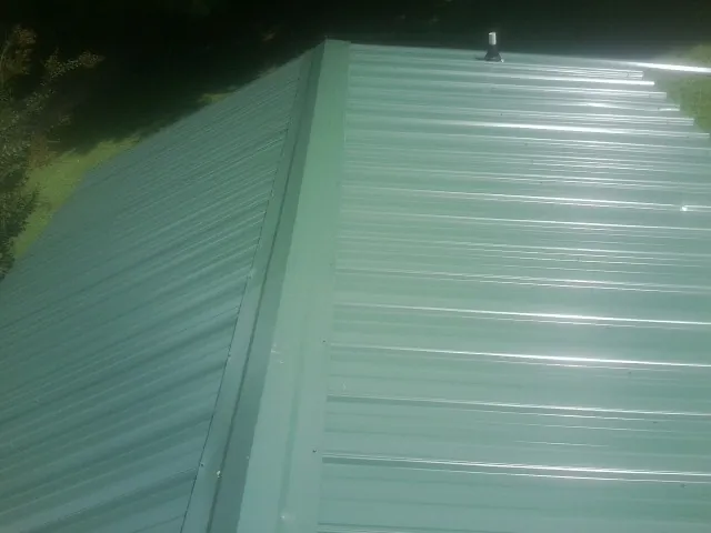 New green metal panels meeting at the ridge of a roof — Flat Roof Repair work by our crew in Bethpage
