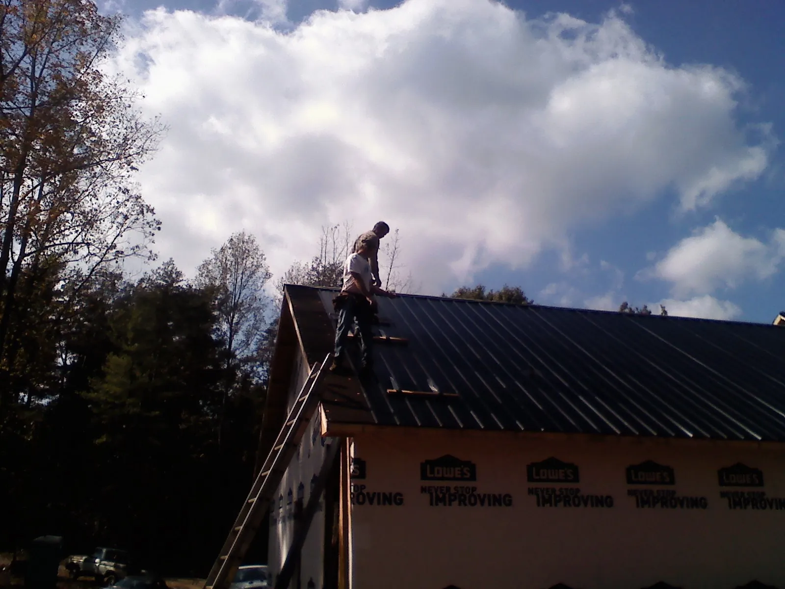 Roofer fastening dark metal panels high against a cloudy sky, from a Roof Inspection job in Bethpage