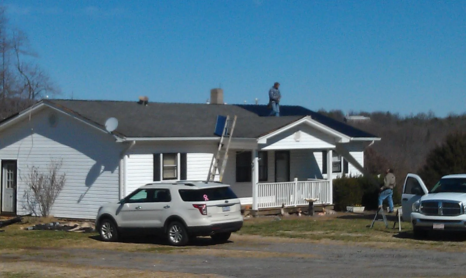 Roofers stripping shingles from a white ranch house roof in Bethpage