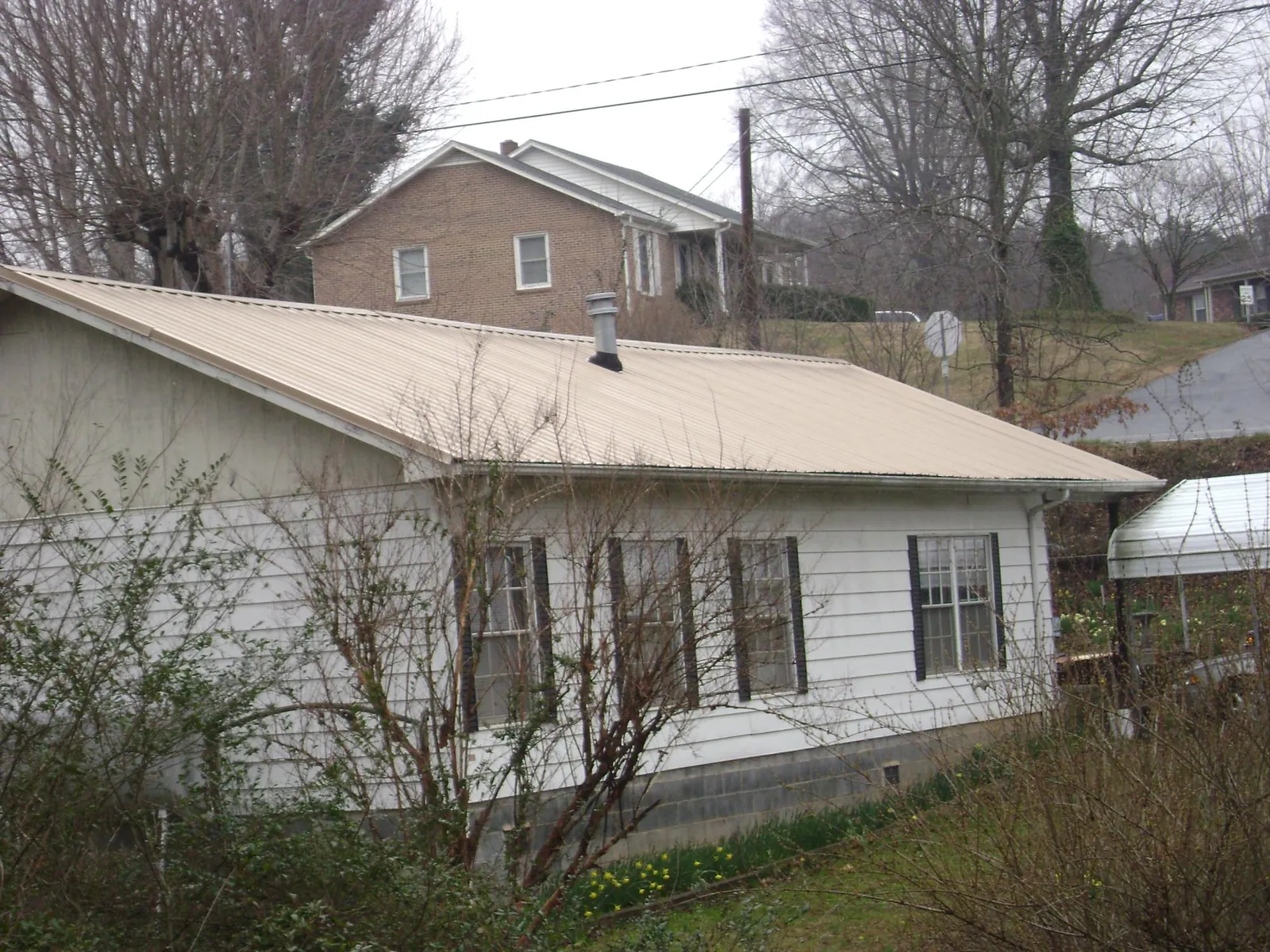Tan metal roof on a white sided house set into a hillside — Commercial Roofing by Roofing Brothers in Bethpage